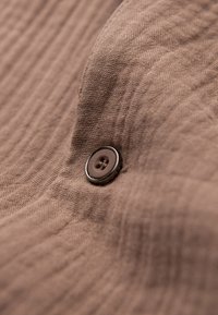Gros plan d'un tissu marron texturé avec un bouton à quatre trous cousu au centre.