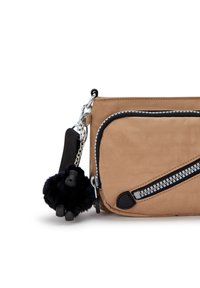 Borsa di tessuto color sabbia con un accento di cerniera nera, caratterizzata da un piccolo charm a pom-pom in pelliccia nera e una tracolla nera. I dettagli della tasca con cerniera sono ben visibili.