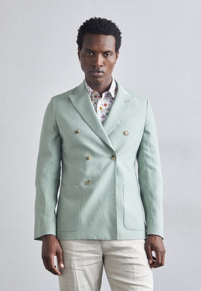 Chaqueta de doble botonadura en verde menta con dos botones decorativos, bolsillos laterales y una tela texturizada. Lleva encima una camisa con estampado floral.