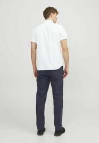 Camicetta bianca a maniche corte con un motivo testurizzato, abbinata a pantaloni blu scuro. La camicia presenta un orlo dritto e un colletto classico.