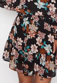 Abito floreale in tessuto trasparente nero, con fiori multicolori in rosa, blu e marrone, dotato di un orlo arricciato e una vita elastica.