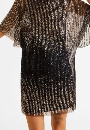Persona che indossa un abito corto nero e oro con paillettes e maniche trasparenti; un tatuaggio floreale è visibile nella parte superiore della coscia.