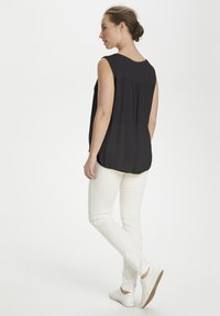 Top sans manches noir avec un décolleté arrondi et un dos plissé, associé à un pantalon blanc ajusté et des baskets blanches.