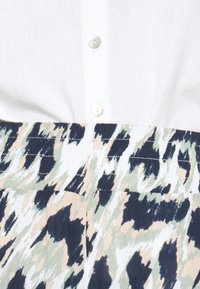 Biała dzianinowa bluzka z zapięciem na guziki przy dekolcie, zestawiona z wzorzystą spódnicą w zielone, beżowe i granatowe fale.