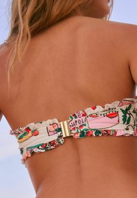 Bikiniöverdel med ett färgstarkt mönster, volanger, justerbara band och ett guldspänne i ryggen. Lätt tygtextur.