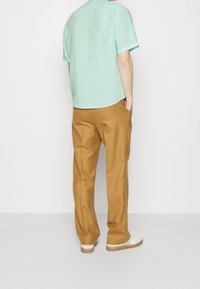 Jasnozielona koszula z krótkim rękawem, luźny krój, zestawiona z beżowymi spodniami. Białe trampki z brązowymi podeszwami. Codzienny strój na ciepłą pogodę.