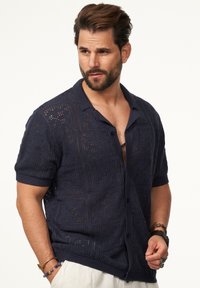 Marineblaues, gestricktes Kurzarmhemd mit Lochmuster, vorderem Knopfverschluss und Kragen. Besitzt Struktur und subtile Designelemente.