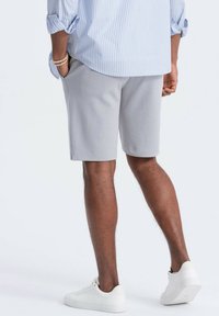 Graue Baumwollshorts mit regulärer Passform, Seitentaschen und glatter Textur, kombiniert mit weißen Sneakers und einem hellblauen gestreiften Hemd.