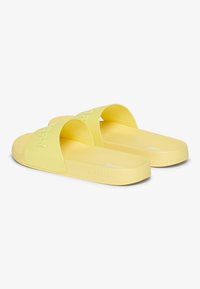 Yellow rubber slide sandals with wide straps, featuring embossed "SUPERDRY" branding. Smooth texture and flat soles for comfort.
