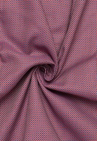 Rood en blauw gestructureerde stof, met een klein geometrisch weefpatroon en een gladde textuur, in een draaiende formatie gedrapeerd.