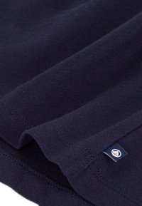 Βαμβακερό ύφασμα σε ναυτικό μπλε με ομαλή υφή, με διπλωμένη άκρη και μικρή ετικέτα λογότυπου στην κάτω δεξιά γωνία.