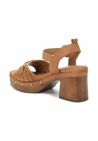 Sandali con tacco in pelle marrone chiaro con parte anteriore intrecciata e borchie metalliche. Presentano un tacco spesso e una cinghia alla caviglia regolabile per una vestibilità sicura.