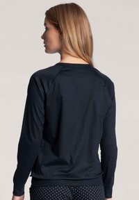 Black sweatshirt with long sleeves, ribbed cuff and hem, smooth texture, crew neck design, and raglan sleeves. Visible polka dot pants.