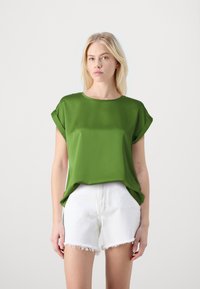 Grønn kortermet bluse med rund hals, laget av glatt stoff, som er paret med hvite frayed denimshorts. Enkel design uten mønstre.