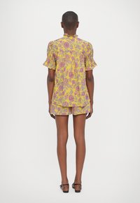 Gul blomstret shorts-sett med puff-ermer og volangkrage. Mønsteret har lilla og rosa blomster på lett stoff.