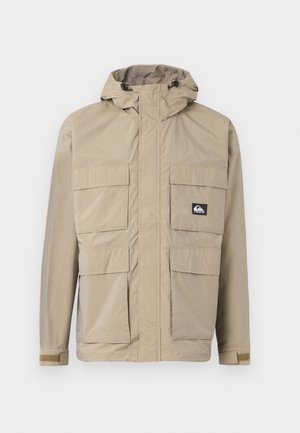 Bež vettetu jope kapuutsiga, millel on ees tõmblukk, neli suurt eesmist taskut ja reguleeritavad mansetid. Tekstuuriga kangas ruudulise mustriga.