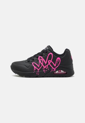 Black sneaker featuring a rubber material, modern design, heart-shaped pink graphic with dripping accents, and a visible air cushion in the sole.