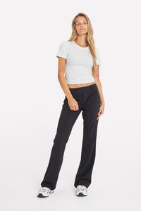 Fehér bordás crop top rövid ujjakkal, fekete elegáns nadrággal és szürke tornacipővel egy fehér háttér előtt.
