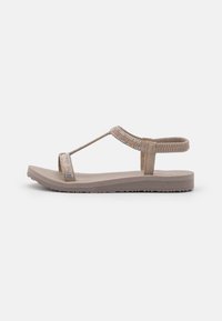 Beige flat sandal featuring a wide strap embellished with multi-colored beads, a T-strap design, and a textured rubber sole.