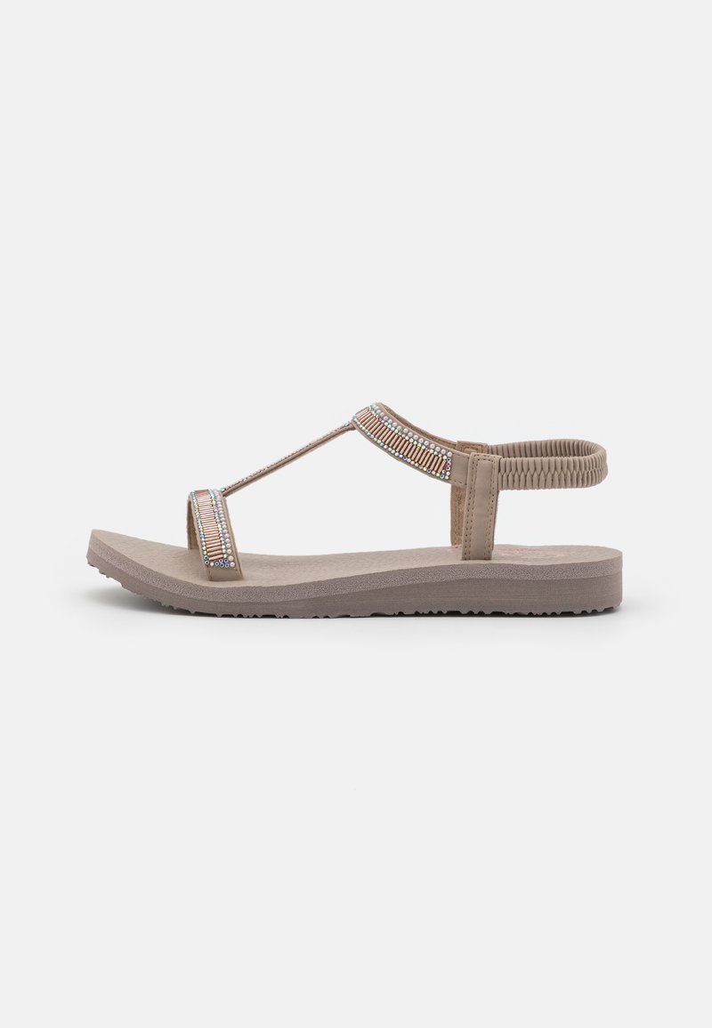 Beige flat sandal featuring a wide strap embellished with multi-colored beads, a T-strap design, and a textured rubber sole.