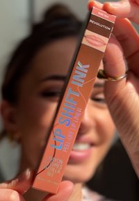 Lip Shift Ink lipliner in een perzikkleurige verpakking, met vetgedrukte tekst, een lippenstiftomtrek en een afpelbare beschrijving.