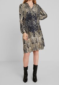 Tiskované šaty s výstřihem do V, dlouhými rukávy a splývavým střihem. Obsahují vzor hadí kůže v tmavě modré, béžové a černé barvě.