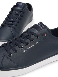 Tamsiai mėlynos sportinės bateliai, pagaminti iš tekstūrinės odos, su plokščiomis raištelėmis, balta guma padais ir šalies šone atspausdintu "TOMMY HILFIGER" logotipu.
