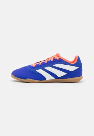 Blaue Sportschuhe mit weißen Streifen und orangen Akzenten. Sie verfügen über ein glattes Stoffoberteil, eine Gummisohle und ein flaches Profil.