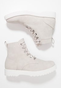 Stivaletti alla caviglia in suede grigio chiaro con suola in gomma bianca, dotati di occhielli in argento, lacci bianchi e una linguetta sul retro.