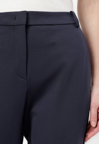 Mornarsko modre klasične hlače iz gladkega materiala; imajo ravno sprednjo stran, slim fit kroj in stranske žepe ter čisto pasovo obrobo.