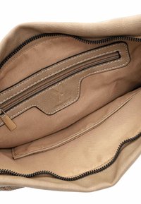 Beige läderhandväska med insida som har en ficka med dragkedja och en tonad foder, med kontrasterande svart söm längs kanterna.