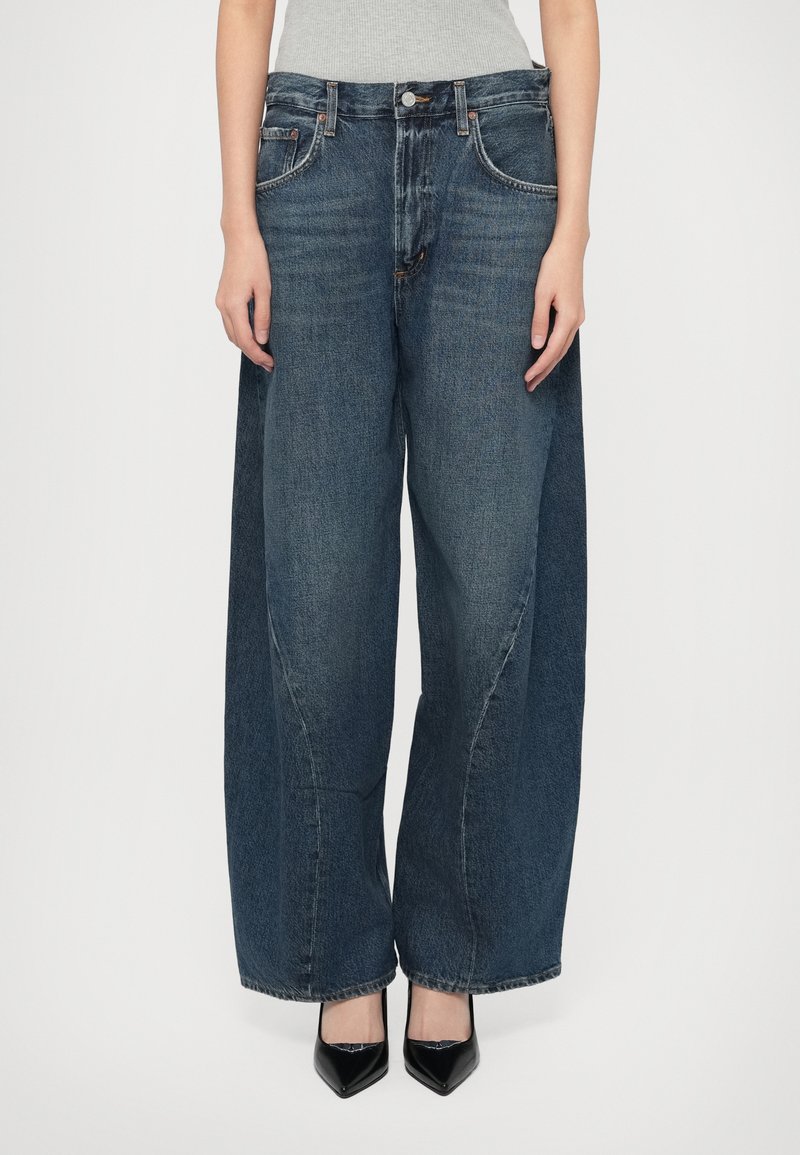 Τζιν με φαρδιά φάσα σε σκούρο μπλε ντένιμ με ψηλή μέση, διαθέτει ραφές σε μπροστινές τσέπες και άνετη εφαρμογή που φαρδαίνει στο τελείωμα.