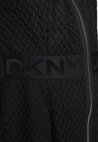 Robe noire DKNY avec un motif en maille texturée, une ceinture en tissu uni et une fermeture éclair sur un côté.