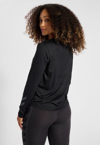 Długi rękaw czarnej sportowej bluzki o gładkiej fakturze; z szarymi akcentami na rękawach. Dobierzono do niej ciemne legginsy z subtelnym wzorem.