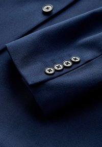 Tengerészkék szövet sima textúrával; ingmandzsettát ábrázol négy fekete gombbal és finom varrási részletekkel.