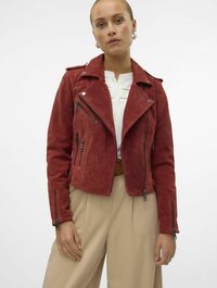Rode suede motorjack met zilveren ritsen, een getailleerde pasvorm, schouderepauletten en een asymmetrische sluiting aan de voorkant. Gecombineerd met beige broeken.
