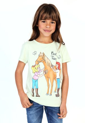 Mädchen trägt ein hellgrünes Shirt mit einem Cartoon-Pferd und zwei Mädchen, die es pflegen, mit der Beschriftung „Bestes Team.“