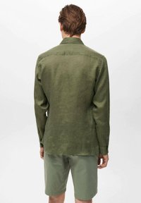 Olive green long-sleeve shirt made of lightweight linen fabric, featuring a straight cut and buttoned cuffs, paired with light green shorts.