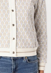 Gemusterte Strickjacke in Creme, mit hellblauen und beigen Blattdesigns, metallischen Knöpfen und einem gerippten Saum mit kontrastierenden Streifen.