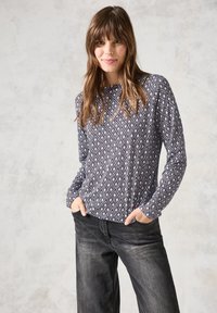 Haut à manches longues avec un motif en losanges bleu marine et blanc, tissu doux, col rond, coupe décontractée ; associé à un jean sombre et ample.