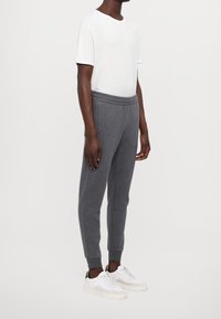 Szare dresy o zwężanym kroju, z elastycznym pasem i bocznymi kieszeniami, zestawione z prostą białą koszulką i białymi sneakersami.