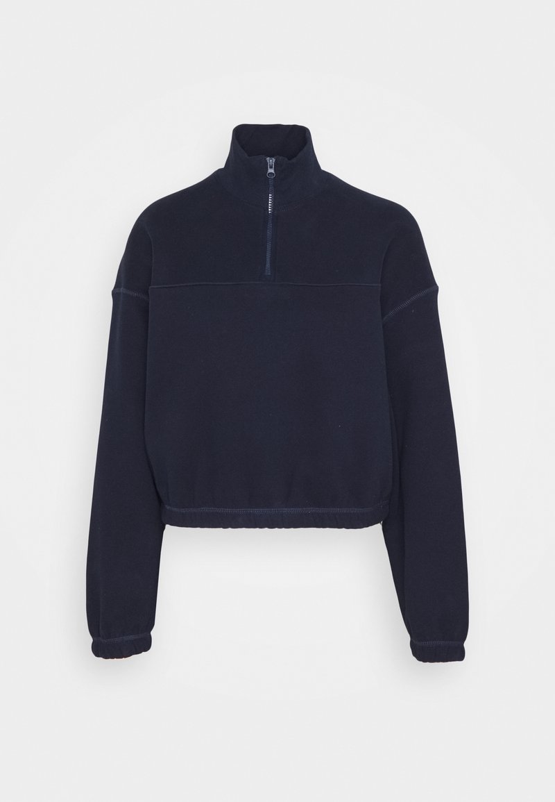 Sweatshirt court bleu marine avec un col haut, une demi-fermeture éclair et des poignets élastiqués. Texture douce avec des coutures plates et un minimalisme dans le design.