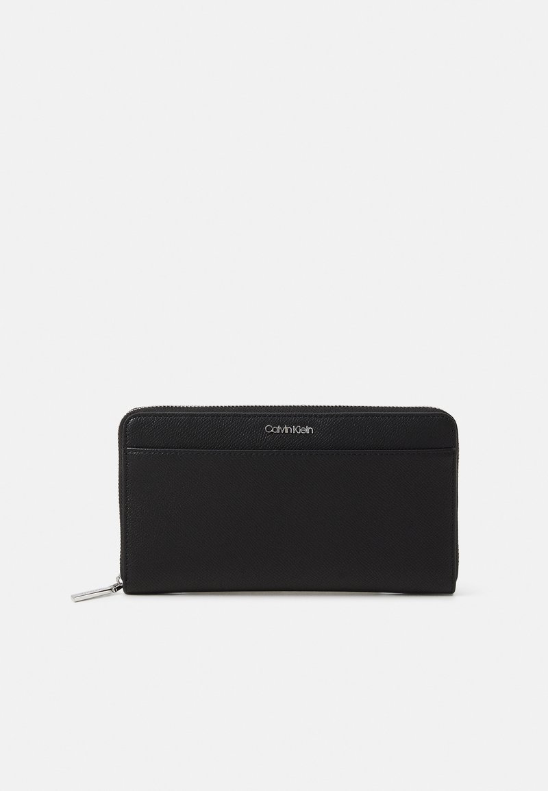 Crna kožna novčanica s teksturiranom površinom, s zatvaranjem na patentni zatvarač i srebrnim Calvin Klein logom sprijeda. Kompaktni i pravokutni dizajn.