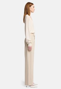 Beige lange mouwtop gecombineerd met beige wijde broek en witte puntige hakken. Zachte textuur; relaxte pasvorm; minimalistisch ontwerp.