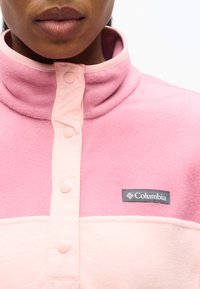 Κοντινό πλάνο ατόμου που φοράει ροζ φλις μπλούζα Columbia με κουμπιά τύπου snap και ψηλό γιακά.