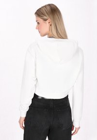 Felpa bianca accorciata con una texture morbida, maniche lunghe e cappuccio. Abbinata a jeans neri a vita alta con tasche posteriori.