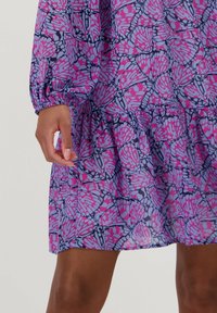 Paarse jurk met een vlinderpatroon in roze en lichtblauw, met lange mouwen en een gerimpelde onderrand. Gemaakt van lichtgewicht stof.