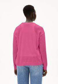 Rosa Langarmpullover aus Baumwolle mit einem lockeren Schnitt, Rundhalsausschnitt und gerippten Bündchen. Kombiniert mit hellblauen Jeans.