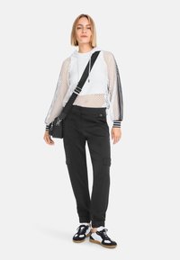 Weißer Hoodie aus Mesh mit Kapuze, schwarze Cargo-Hosen mit Seitentaschen und schwarze Turnschuhe mit weißen Akzenten. Einfaches, sportliches Design.