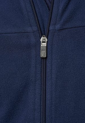 Tengerészkék fleece dzseki teljes elöl cipzárral. Texturált anyag és ezüst cipzárhúzó logóval. A cipzár nyomvonala látható a varrás mentén.